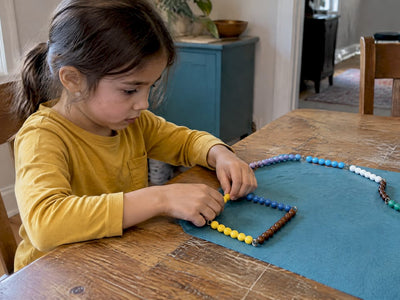Child folds a colored bead chain into a square