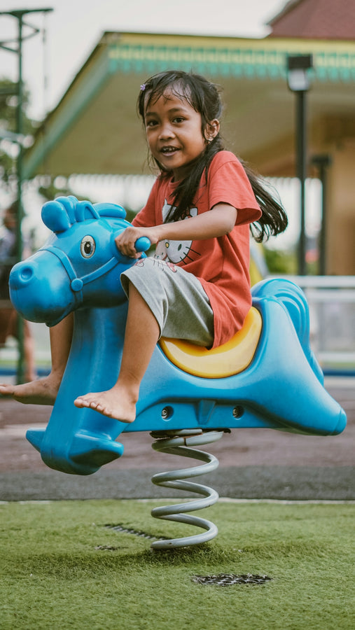 A happy girl rides a spring horse at the park.