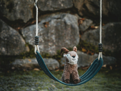 A stuffed fox sits on a swing outdoors.