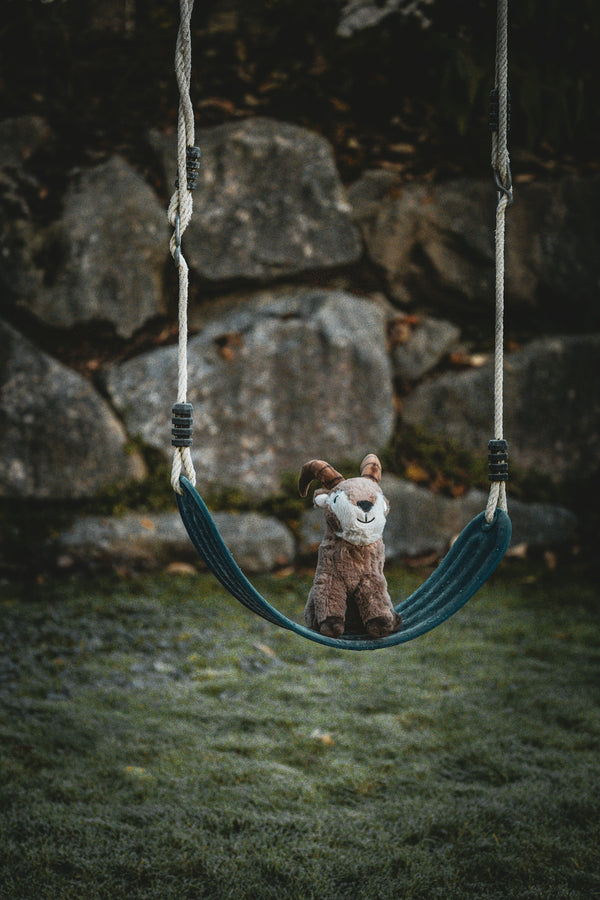 A stuffed fox sits on a swing outdoors.