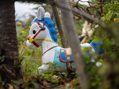 A white rocking horse with blue mane sits outdoors.