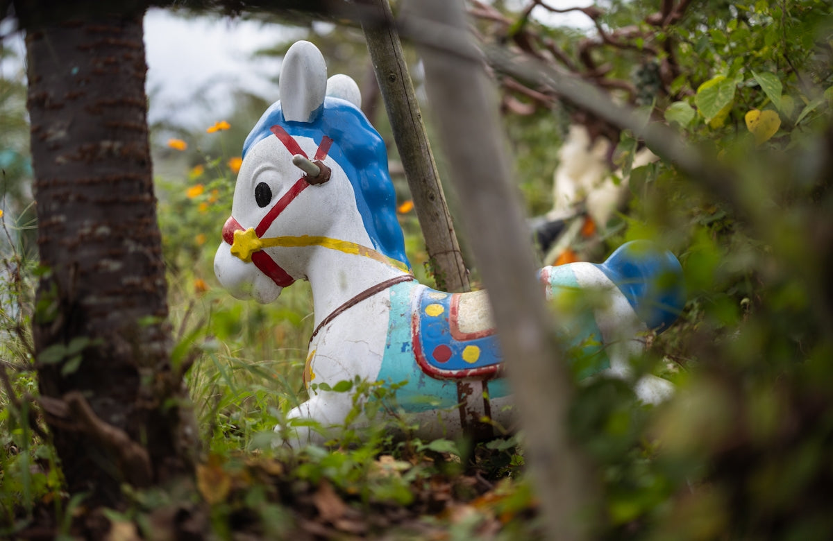 A white rocking horse with blue mane sits outdoors.